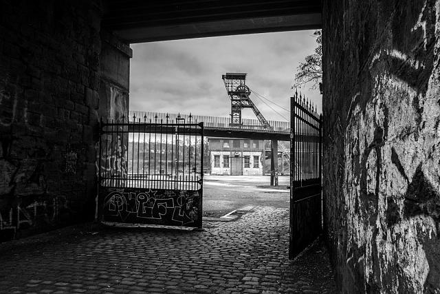 Encadré dans une arche du pont, derrière un portail en fer, le chevalement du puits Couriot