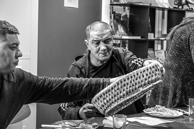 Un homme tend la panière à pain à un autre, qui se sert.